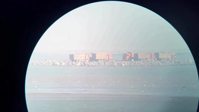 2021年12月，自然之友赴蓝色海湾项目施工现场调研，几辆土方车正驶入工地。图片为望远镜视野。  受访者供图
