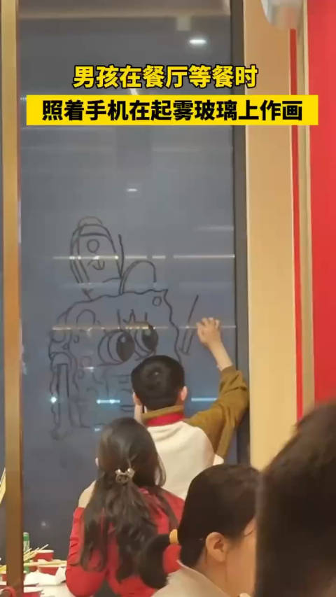 男孩在餐厅等餐时,照着手机在起雾玻璃上作画
