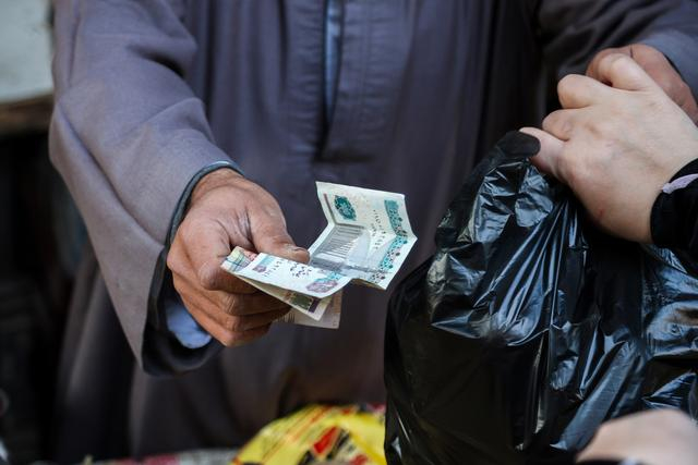 当地时间2024年3月7日，埃及开罗，在Sayyida Zeinab食品市场，一名小贩将埃及镑钞票交还给顾客。视觉中国 图