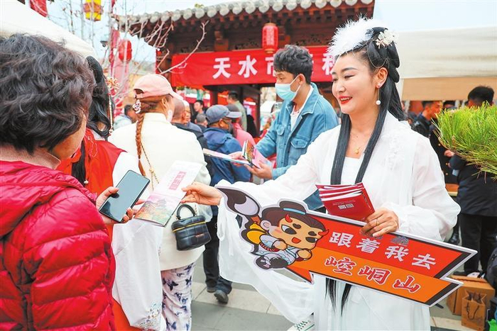 工作人员在天水麻辣烫吃货节农特产品展示区给游客发放文旅宣传手册。