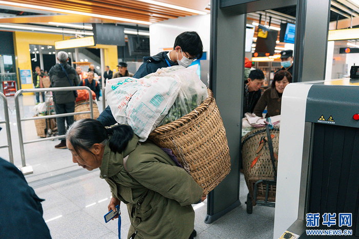 △菜农们背着背篓，在工作人员的引导下过安检进站乘车。新华网 耿骏宇 摄