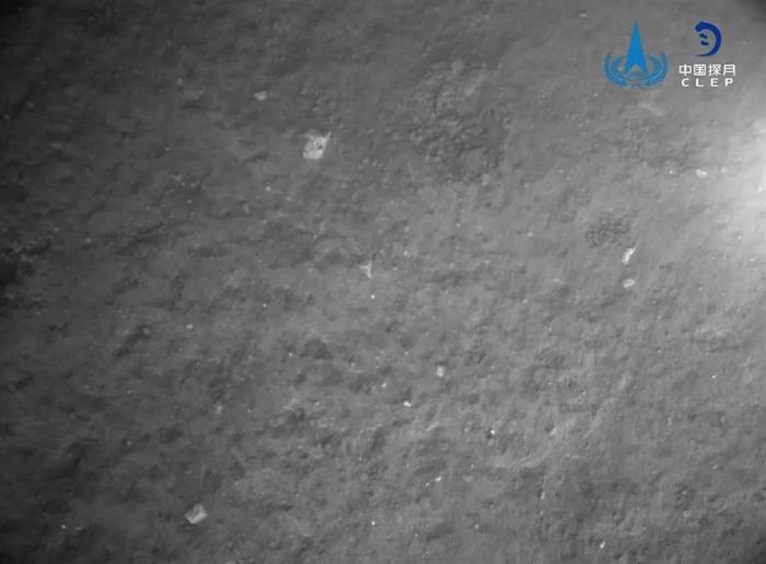 由降落相机在着陆器安全着陆后拍摄，图像显示着陆器底部相对平坦，分布有少量亮色石块。国家航天局供图