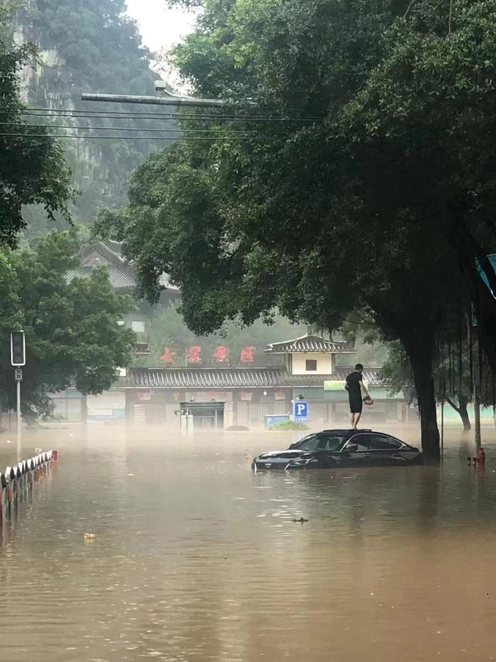 6月19日，因水位上涨，桂林市一司机爬上小轿车车顶等待救援。受访者供图