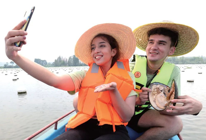 在浙江省德清县阜溪街道龙胜村小山漾农业文化遗产地区域，外国留学生在用手机直播珍珠蚌开蚌取珠过程