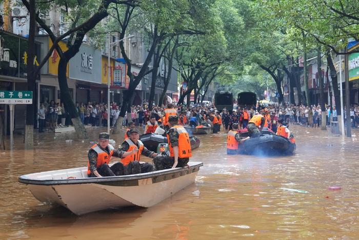 2024年7月2日，湖南平江县，救援人员乘坐冲锋舟前往受灾地区，身后站着广大的市民群众。中新社记者 杨华峰/视觉中国 图