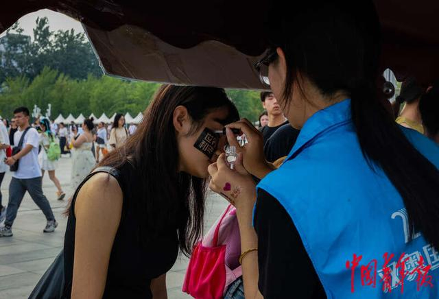 7月19日，北京，奥林匹克公园，工作人员在演唱会观众的脸上贴闪粉纹身贴，字样为歌手薛之谦常挂在嘴边的口号。林小渠/摄