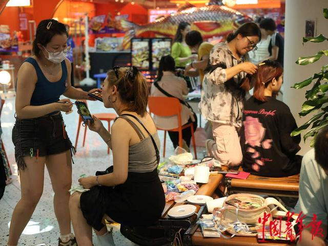 7月19日，北京，新奥购物中心，编发化妆的摊主在空闲的凳子上开始自己的生意。林小渠/摄