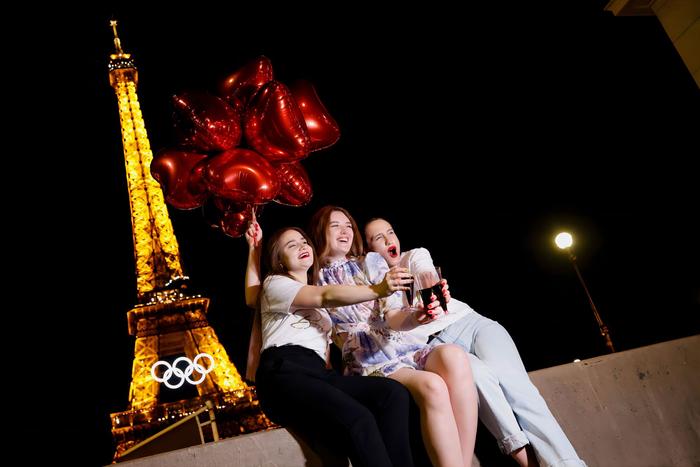 当地时间2024年6月7日，游客们手持红色的心形气球和红酒在装饰着奥运五环的埃菲尔铁塔前摆姿势。 