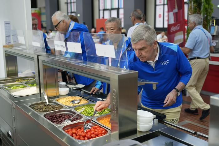 7月22日，国际奥委会主席巴赫（前）品尝奥运村内的食物。 新华社发（Pool照片/大卫·戈德曼）