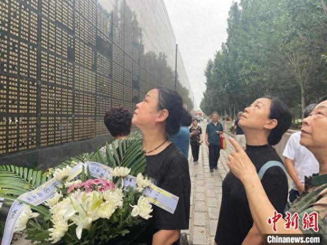 7月27日，在河北唐山地震遗址纪念公园地震纪念墙下，几名唐山大地震幸存者在寻找墙上罹难亲人的名字。白云水 摄