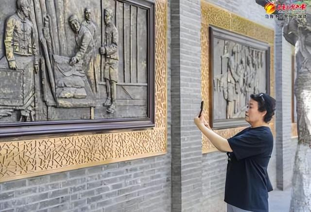 　　8月13日，在位于天山区的明德路，行人王丽用手机拍摄“工夫市”主题浮雕墙。 记者米热扎提·木塔力甫摄