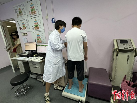     首都医科大学附属北京儿童医院减重门诊诊室里，患儿在医生的帮助下站上人体成分分析仪。中青报·中青网见习记者 谭思静/摄