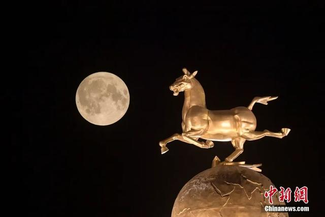 图为圆月从四川省广安市上空升起，与城市地标“马踏飞燕”形成一道美丽的风景线。图/ICphoto
