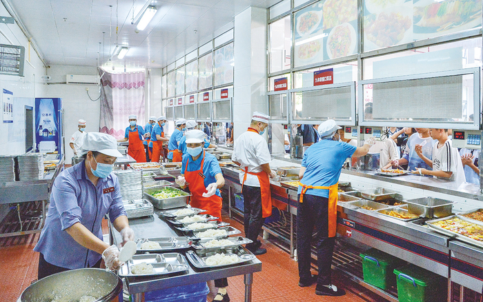     ▲在南宁市新民中学食堂操作间，工作人员有序分餐。    本报记者黄维业 摄