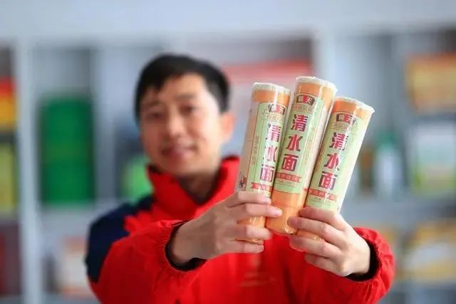 ▲东阳村驻村第一书记朱强，展示村里面条厂生产的黄关面条。资料图