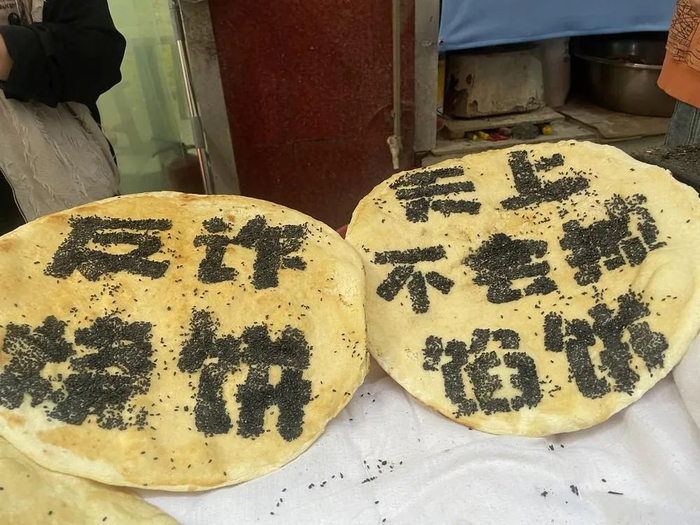 大烧饼上用黑芝麻撒上了“天上不会掉馅饼”几个大字，提醒买烧饼的街坊