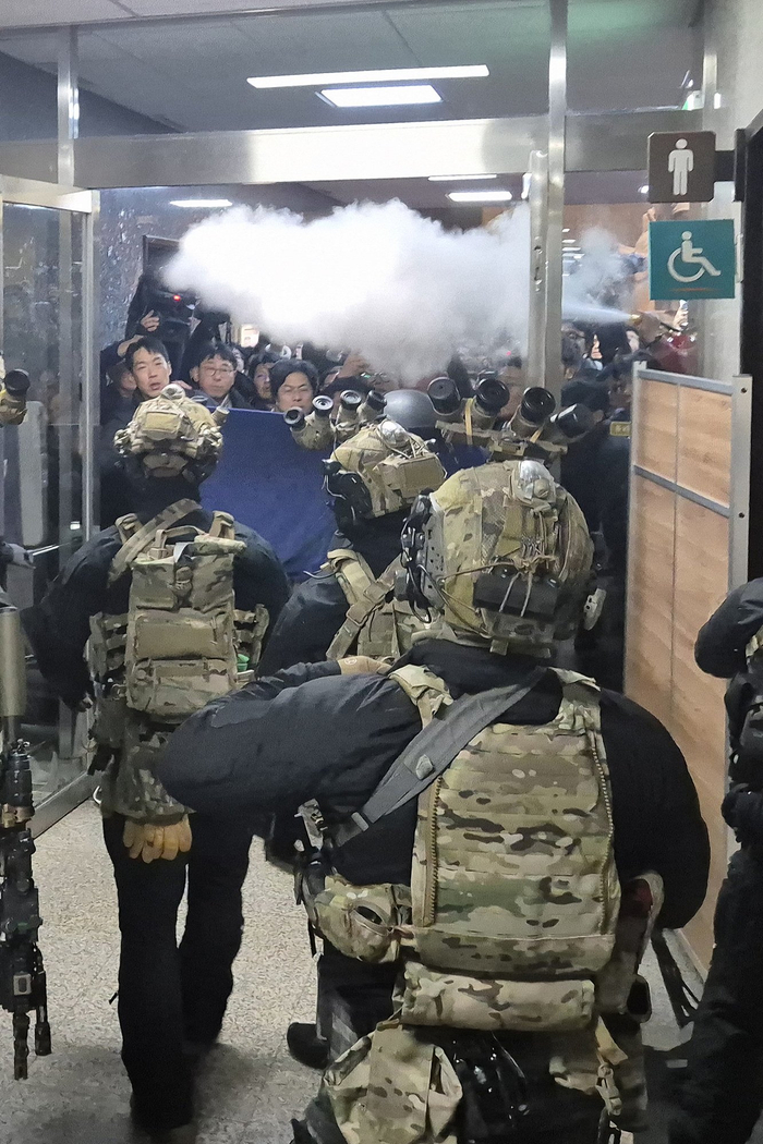 当地时间12月4日，韩国首尔，国会工作人员试图喷洒灭火器阻止武装军队进入国会大厦。