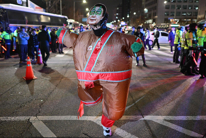 当地时间2024年12月4日，韩国首尔，身着韩国总统尹锡悦面具服装的男子在国会大厦外跳舞。