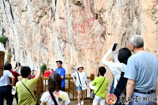 资料图片：来自各地的游客正在世界文化遗产——广西崇左花山岩画前游览参观和拍照留念。广西云-广西日报记者 周贻刚 摄