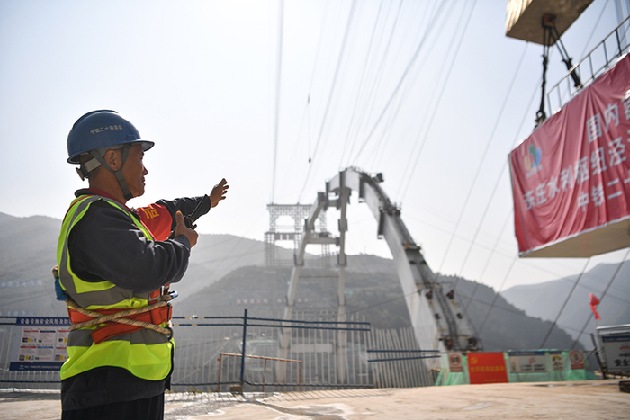 2023年10月10日，中铁二十局工人在陕西东庄水利枢纽泾河大桥施工现场指挥吊机进行吊装作业。新华社记者 张博文 摄