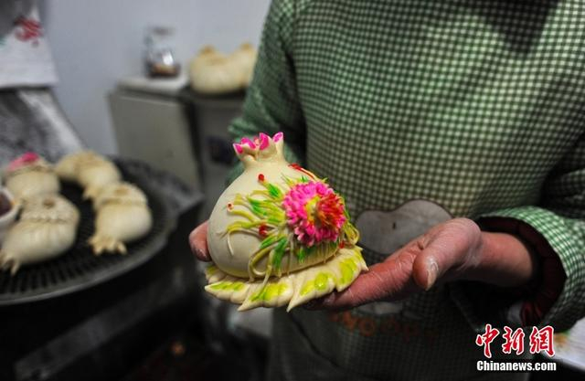 图为山西闻喜，一位花馍艺人端着一个制做完成的石榴花馍。