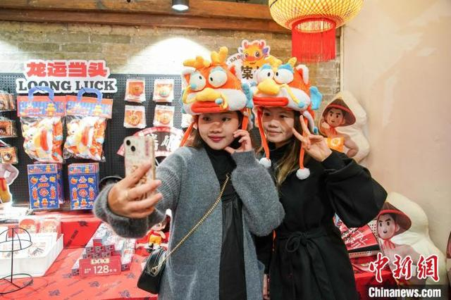 2月7日，广西南宁市宾阳县宾州古城南街一家炮龙文创产品店，两名顾客头戴该店的“龙咚锵”炮龙棉帽自拍。陈冠言 摄