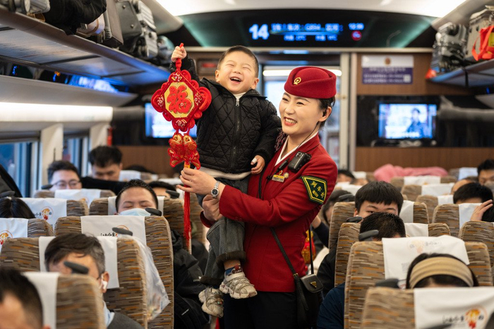 在G894次南昌西开往北京西的列车上，乘务员抱着小旅客，同举福字挂饰。张萌飞 摄