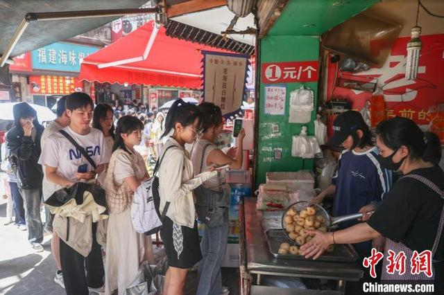 5月2日，江西南昌东湖区，游客在大士院老街的一家商铺前排队购买南昌特色美食白糖糕。中新社记者 刘力鑫 摄