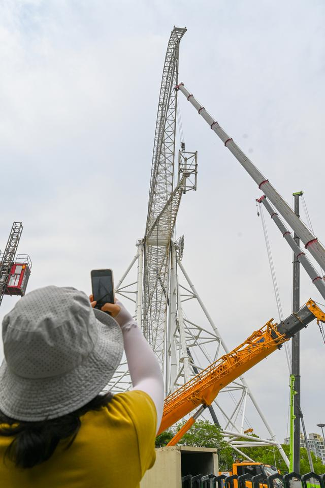 2025年5月15日，上海，刘女士用手机拍摄正在拆除的摩天轮。澎湃新闻记者 朱伟辉 图