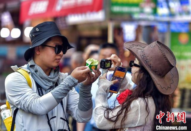 5月21日，新疆乌鲁木齐市和田二街，游客在街头拍摄刚刚购买的手工冰淇淋。中新社记者 刘新 摄
