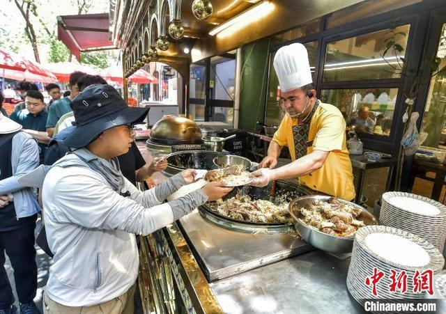 5月21日，新疆乌鲁木齐市和田二街，游客排队品尝抓饭。中新社记者 刘新 摄