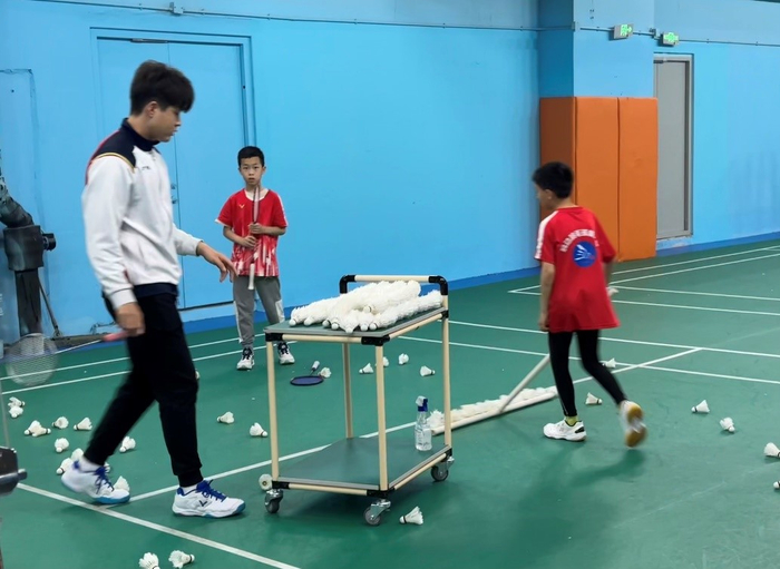 图为羽动羽毛球球馆内，教练带领学员回收场地上的羽毛球。