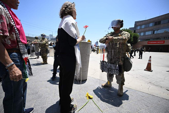 当地时间2025年6月10日，美国加州洛杉矶，一名示威者在抗议中手持鲜花，准备献给在联邦大楼外执勤的国民警卫队士兵。