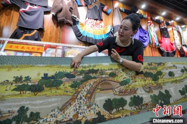 6月10日，在四川省马边彝族自治县马边花间刺绣专业合作社工作坊里，乔进双梅介绍彝绣作品《清明上河图》。中新社记者 王磊 摄