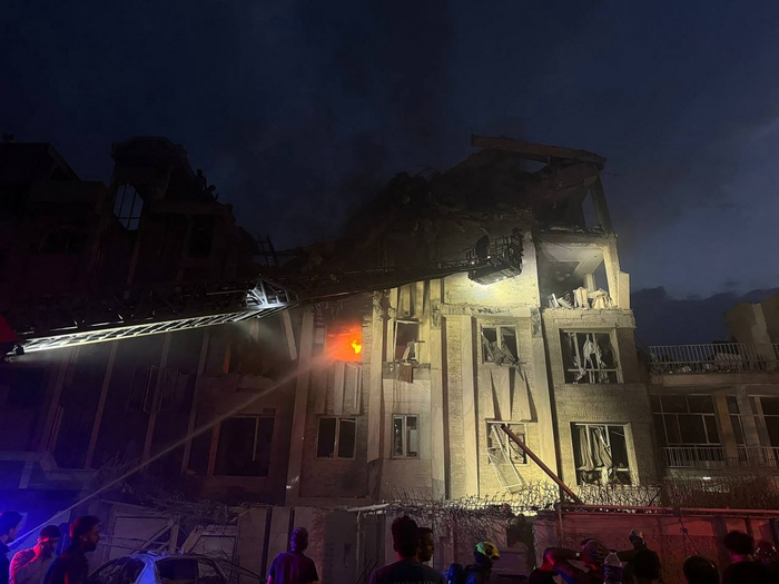 当地时间2025年6月13日，伊朗德黑兰，一栋建筑在以色列空袭后起火，现场有围观者和救援队伍。