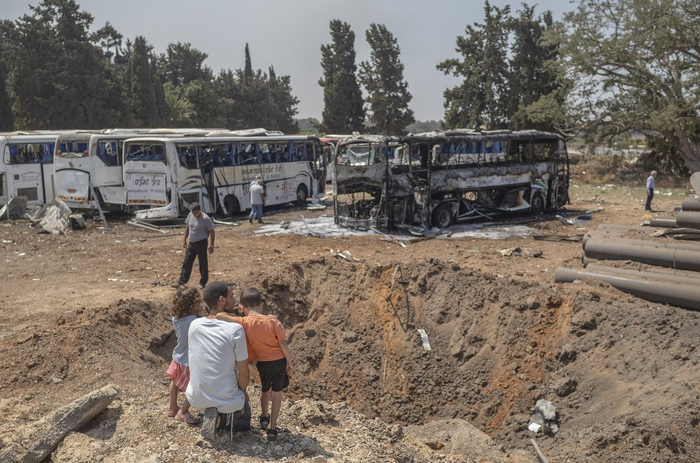 当地时间2025年6月17日，以色列荷兹利亚，一位父亲和孩子在被伊朗导弹损坏的公交车前。