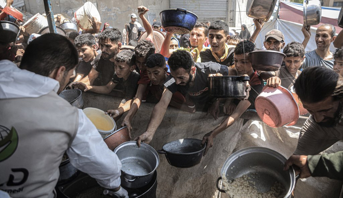 当地时间2025年6月12日，加沙地带加沙城，流离失所的巴勒斯坦人聚集在一起，领取一家慈善机构分发的免费热餐。