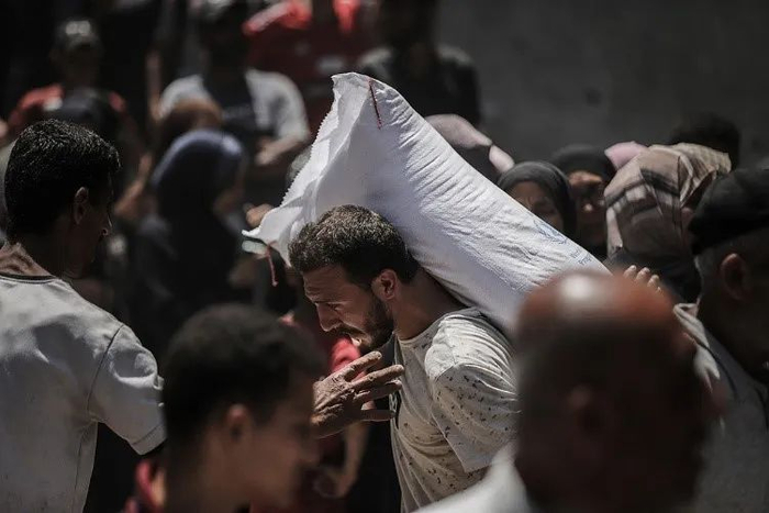 当地时间6月26日，一名巴勒斯坦男子背着从世界粮食计划署分发点领到的一袋面粉。图源：视觉中国