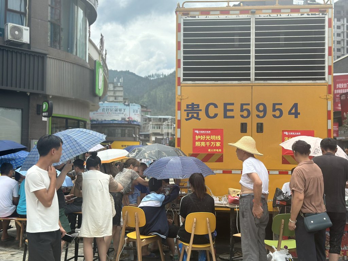 居民们打着遮阳伞围坐在应急发电车旁边为手机充电。