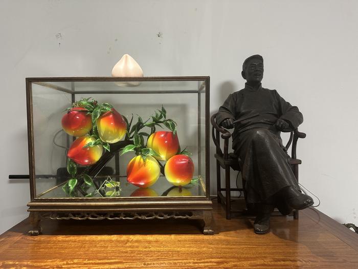 杨少华房间的柜子上摆放着桃子工艺品，旁边是泥塑大师为他塑的像。新京报记者 李冰洁 摄