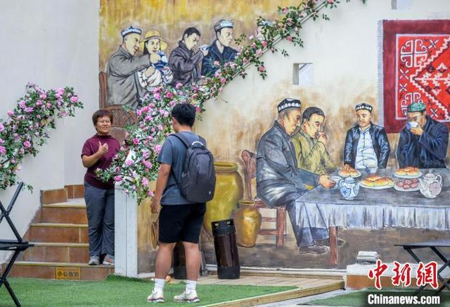 7月17日，新疆乌鲁木齐市大巴扎步行街，游客在描绘新疆老茶馆的彩绘墙前留影。中新社记者 刘新 摄