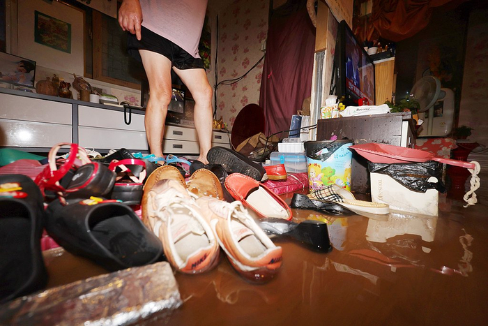 当地时间2025年7月17日，受暴雨警报影响，韩国光州白云广场附近一处商铺被水淹没，店主正在进行排水作业。