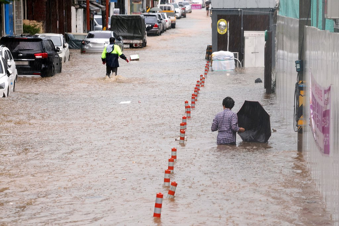 当地时间2025年7月17日，韩国光州，在暴雨袭击该市后，人们在被洪水淹没的街道上艰难前行。