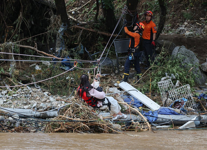 当地时间2025年7月20日，韩国京畿道加平郡，一名市民在被洪水冲毁的道路上，通过绳索被从一处露营地救出。
