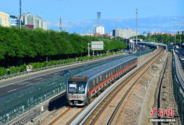 北京地铁列车行驶在八通线上，远处北京CBD建筑群清晰可见。罗春晓 摄