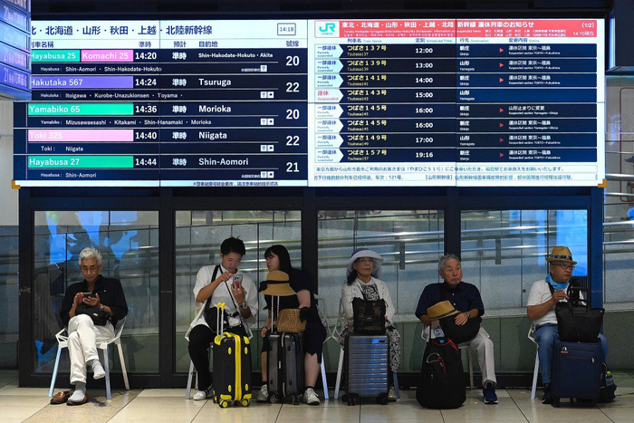 当地时间2025年7月30日，日本东京，东京车站内，旅客们在显示部分列车因海啸警报取消的指示牌下等候。视觉中国 图