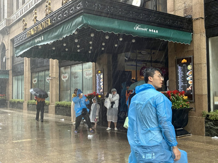 7月30日，游客在和平饭店屋檐下等待雨停间隙。