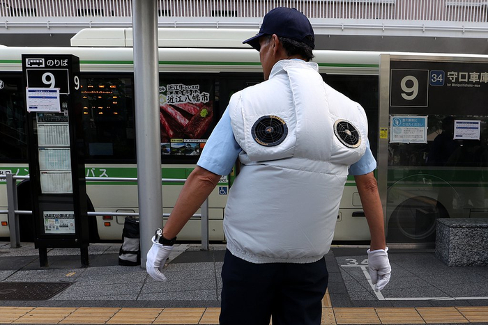 当地时间2025年7月31日，日本大阪梅田区，一名保安在公交车站穿着带风扇的降温背心。