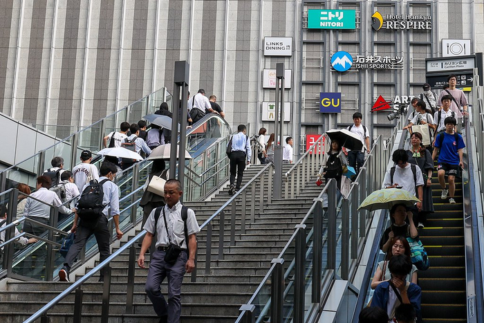 当地时间2025年7月31日，日本大阪梅田区，早高峰通勤者打伞走在人行天桥的台阶上。
