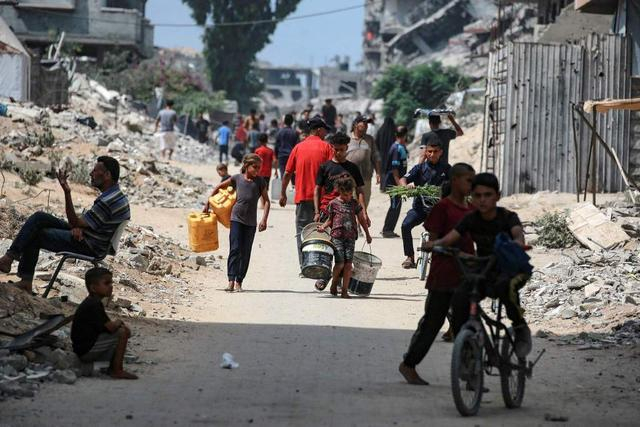 当地时间2025年8月8日，加沙城，巴勒斯坦民众提着大桶和水桶走在被战争破坏的街道上。视觉中国 图